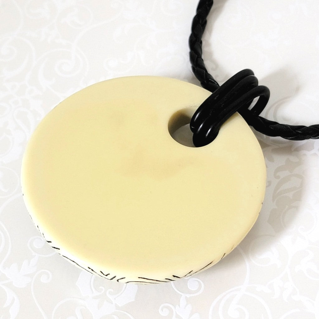 Closeup back view of a large resin pendant on a Chicos necklace, with black braided cord.