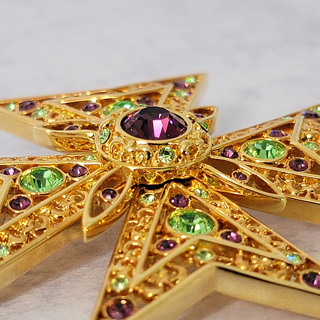 Purple and green crystal rhinestones on a gold tone brooch.