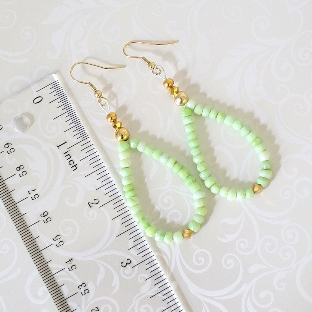 Green gemstone dangle earrings, with gold crystal accents, shown next to a ruler.