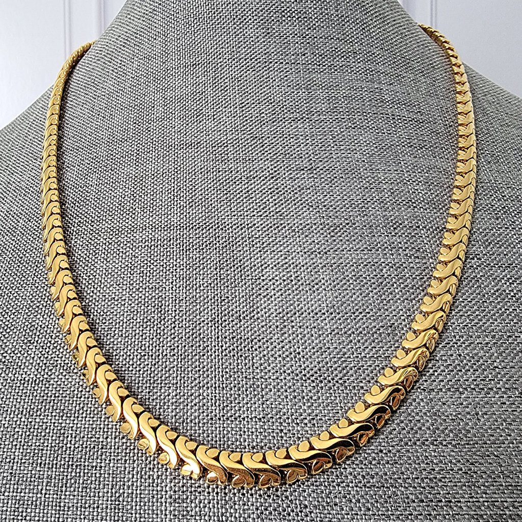 Fancy link gold tone chain necklace on a display stand.