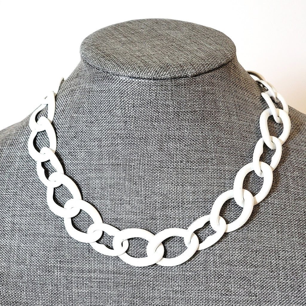 White enamel chain necklace on a gray display stand.