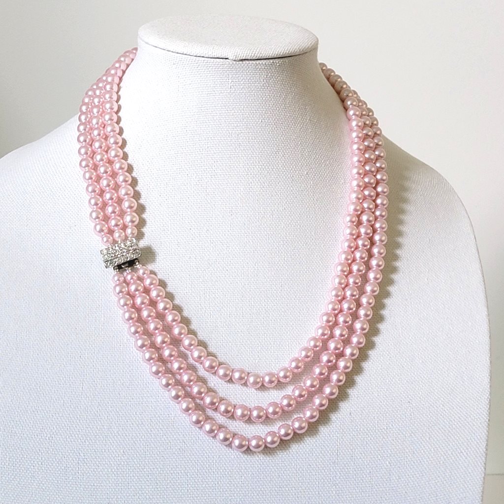 Pink three strand faux pearl necklace, with rhinestone clasp, on a display stand.
