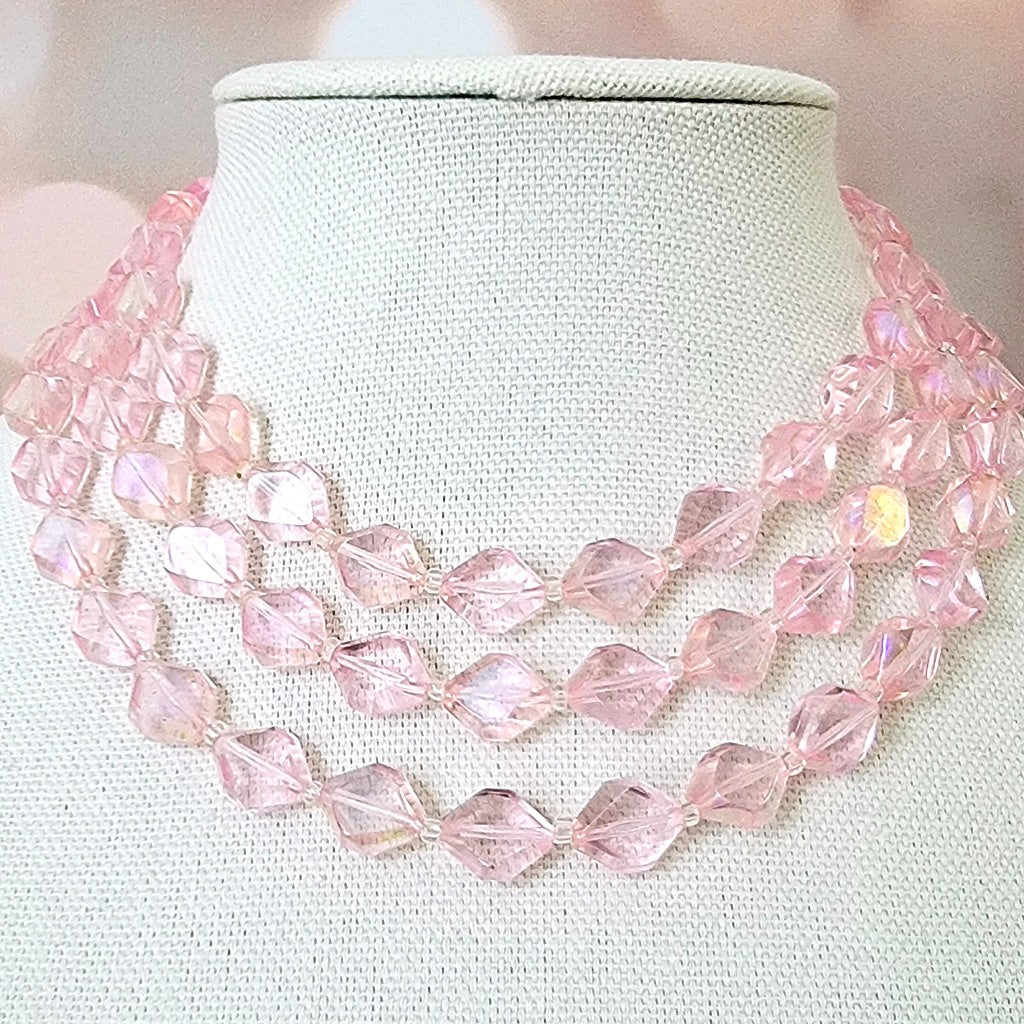 Three strand vintage pink necklace on a display stand.
