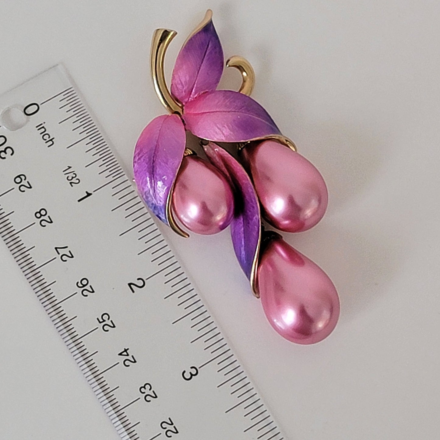 Large pink faux pearl pin next to a ruler.