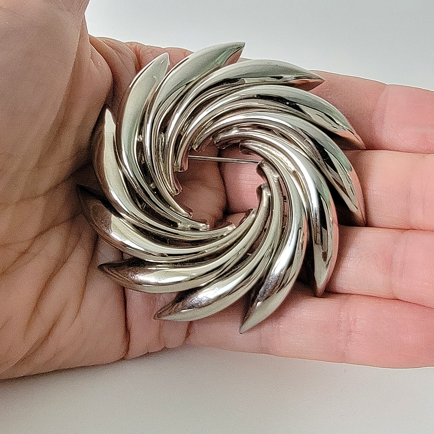 Vintage silver tone wreath pin in hand.