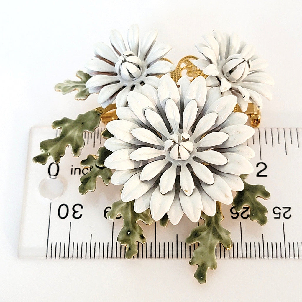 White enamel flower brooch with a ruler.