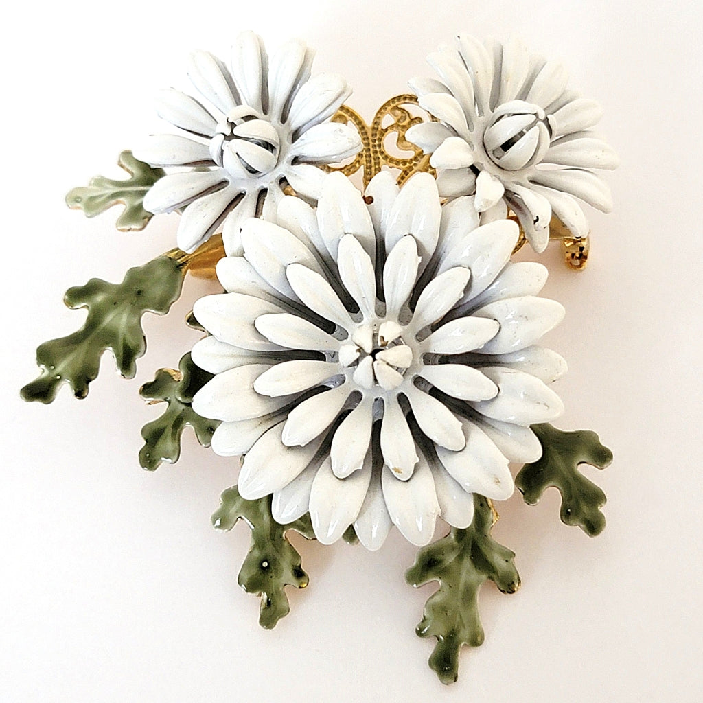 Vintage white flower brooch with green leaves.