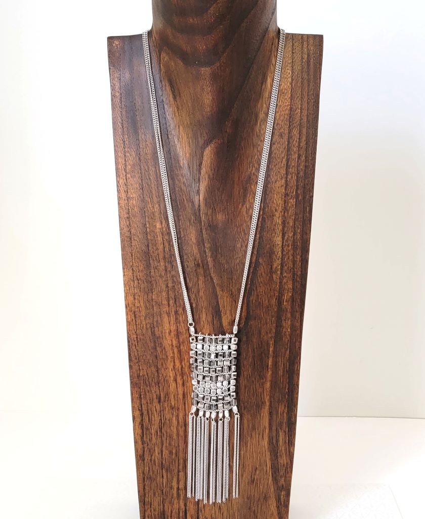 Kenneth Cole long silver tone modernist fringe necklace on a display stand.