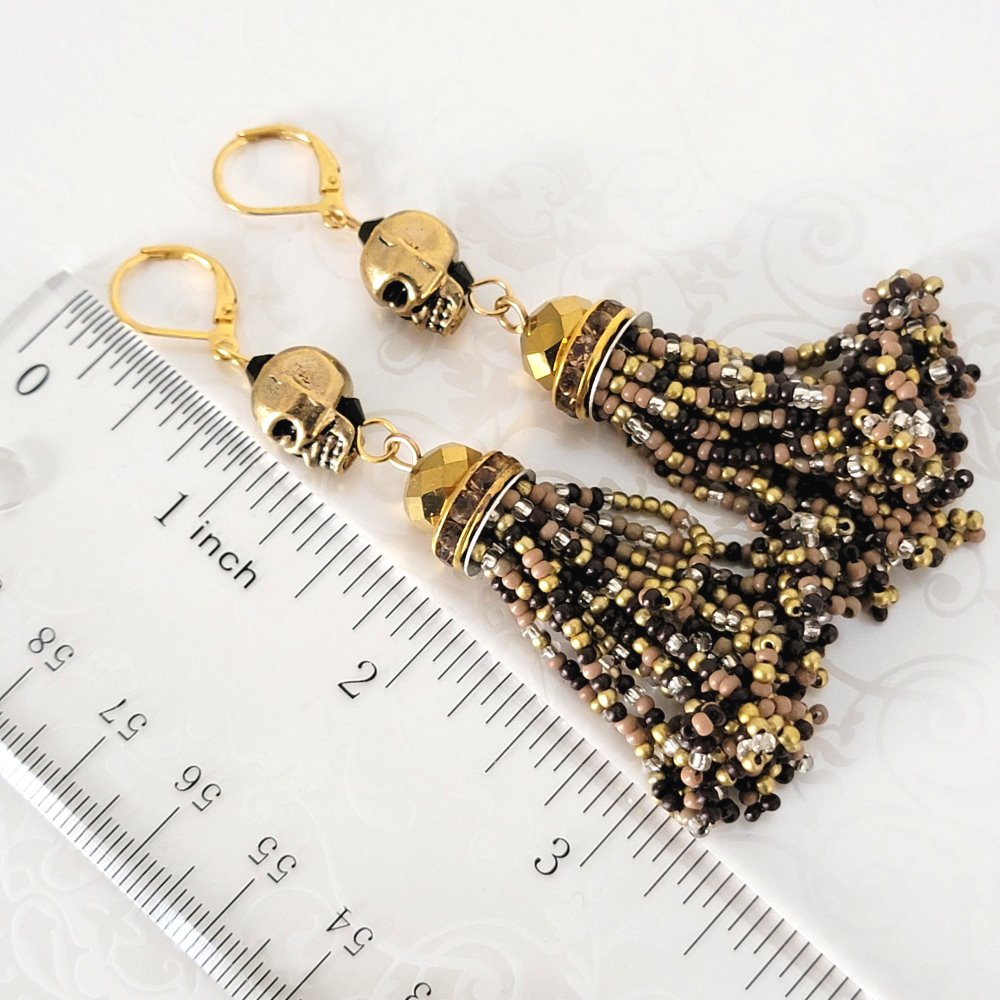 Long gold tone skull dangle bead tassel earrings, next to a ruler.