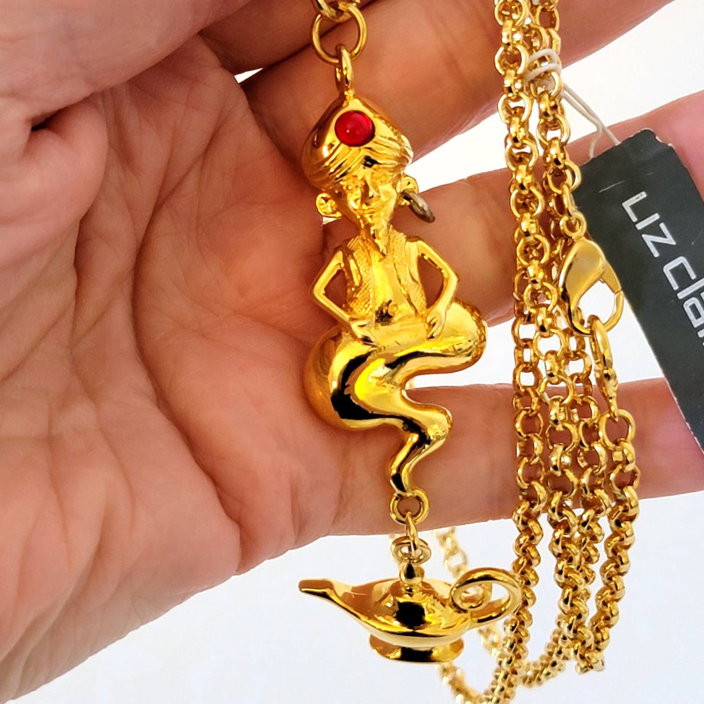 Closeup view of a LCi gold tone genie pendant, shown in hand, for size comparison.