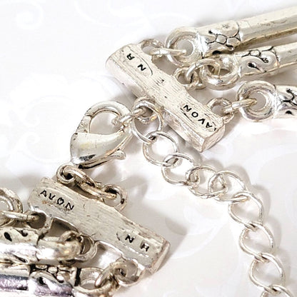 Closeup view of a silver tone, Avon necklace clasp, showing signature marks.