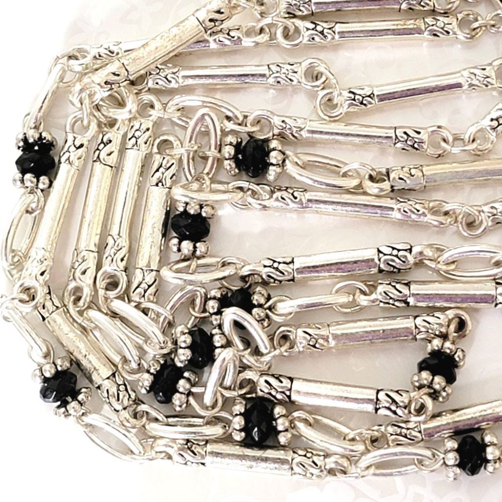 Closeup detailed view of a silver tone Avon necklace, with black accent beads.