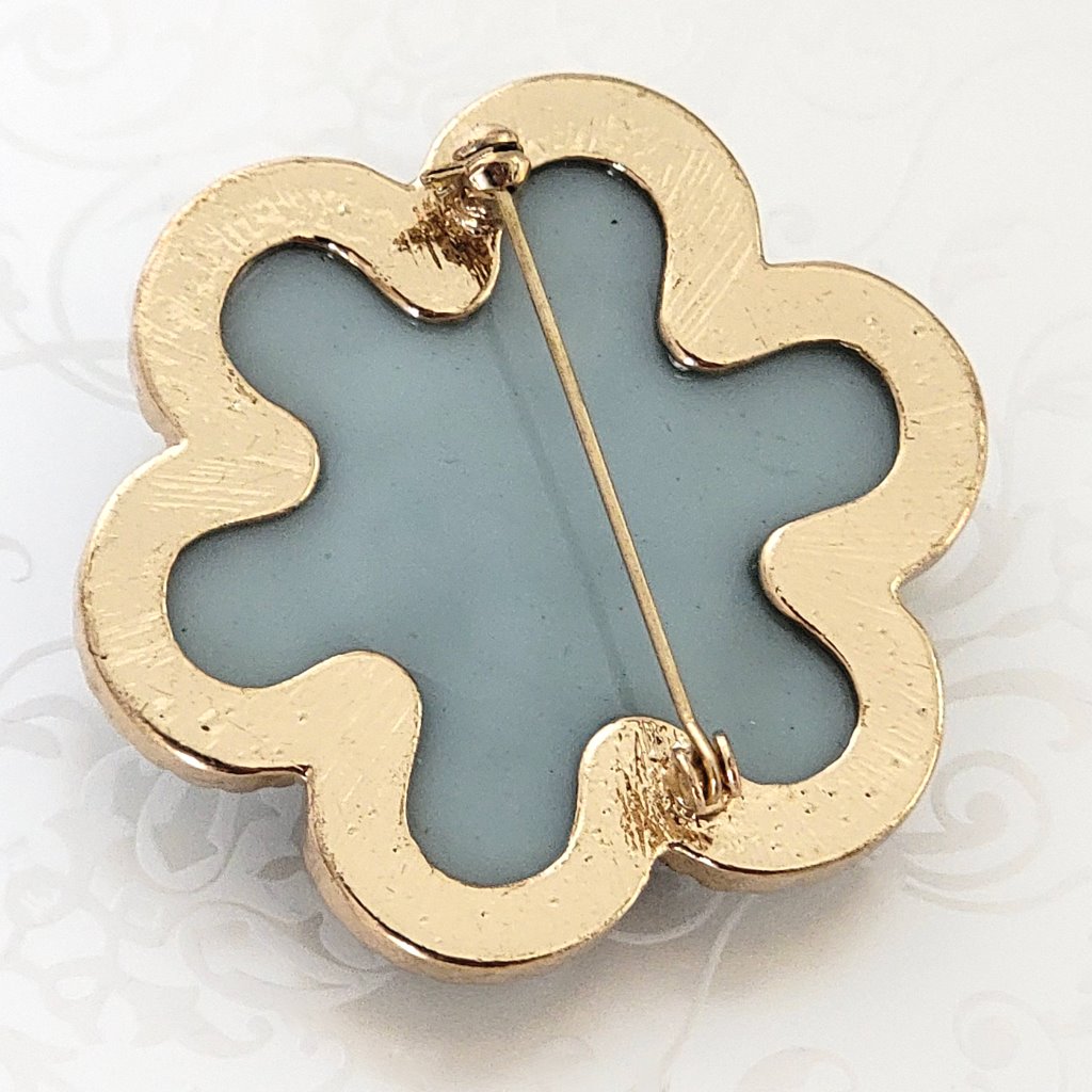 Back view of a blue acrylic flower brooch, showing the gold plated metal setting and clasp.