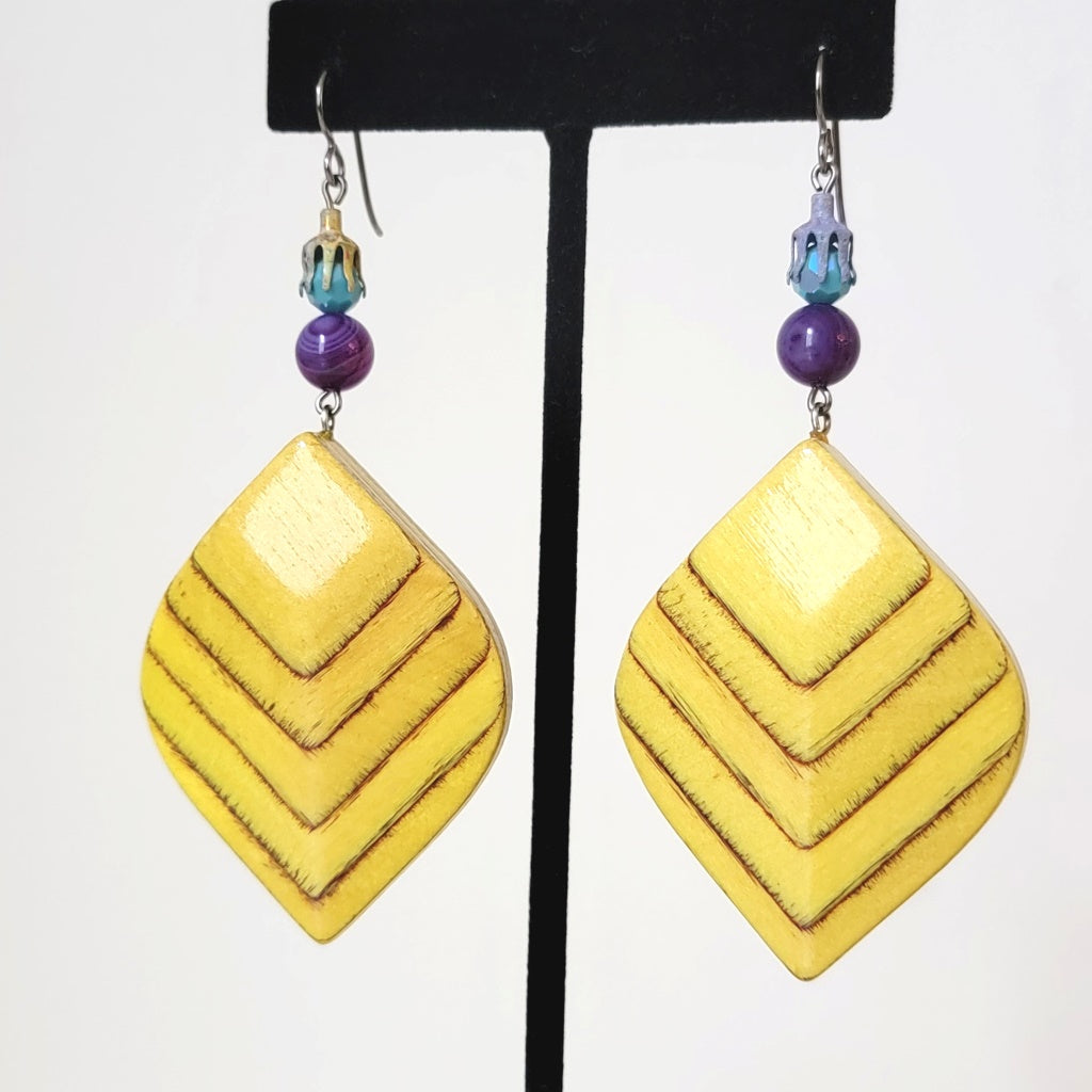 Large yellow wood chevron pattern earrings, with purple stones. shown on a display stand.