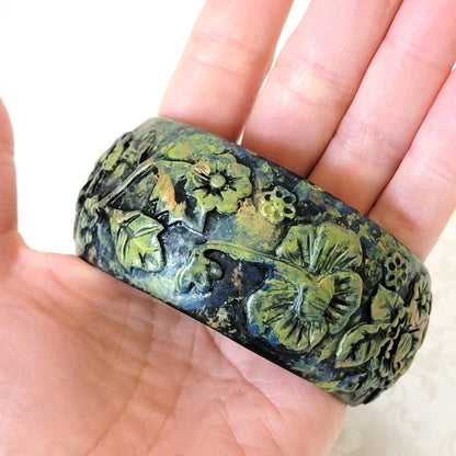 Wide flower bracelet, in black and green molded resin. Shown in hand, for size comparison.