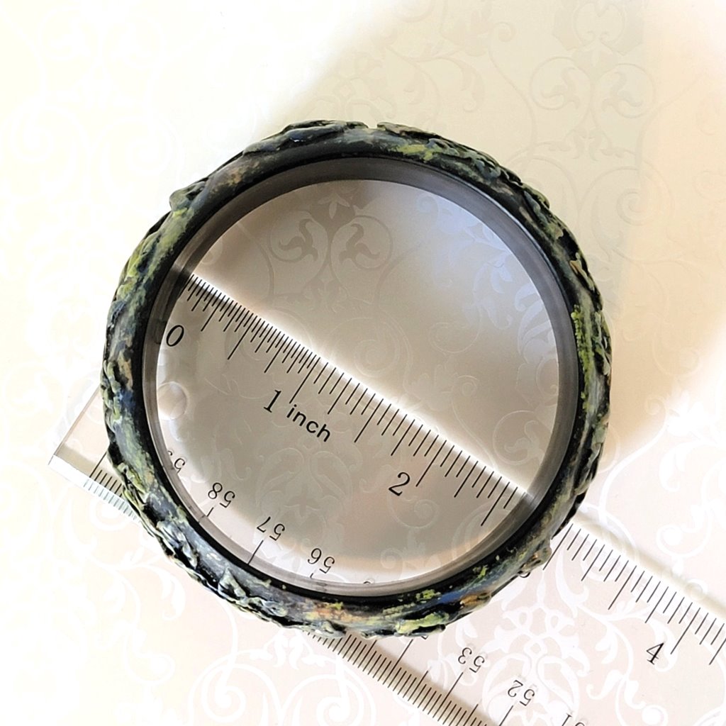 Top view of a black plastic bangle bracelet. Shown next to a ruler.