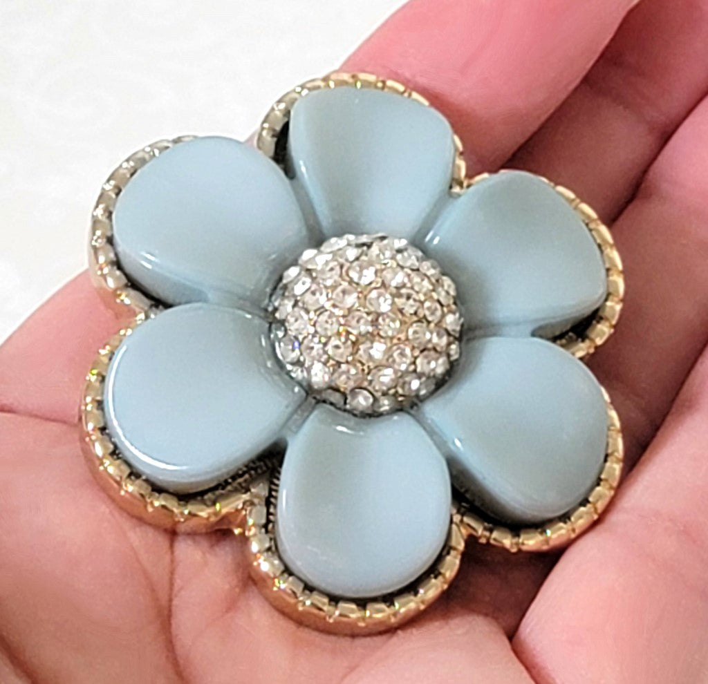 Pale blue plastic flower brooch, with glass rhinestones. Shown in hand, for size comparison.