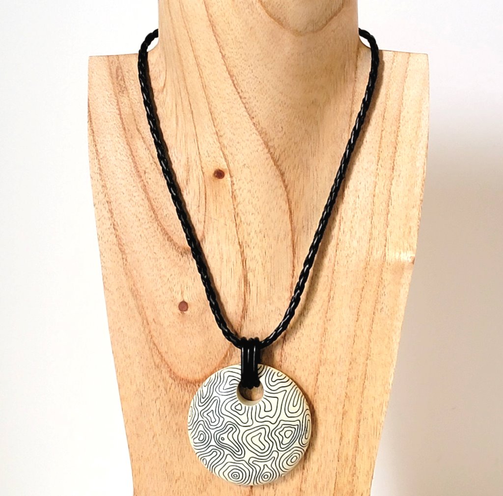Chicos, abstract swirl pendant necklace. Giant circle, on a black braided leather look cord. Shown on a wooden display stand.