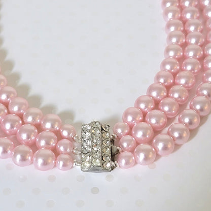 Close-up view of a rhinestone clasp on a vintage pink faux pearl necklace.