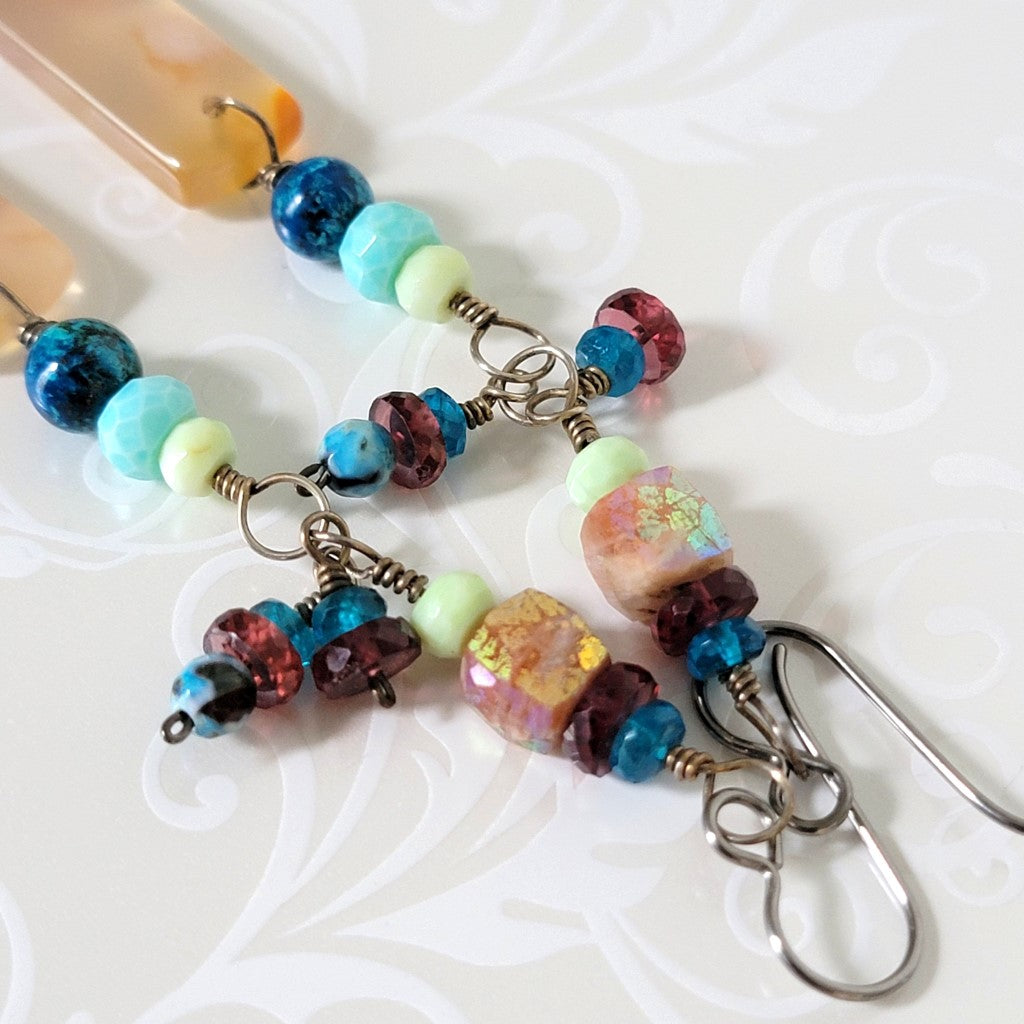 Close-up view of garnet, apatite, sunstone, and opal beads on dangle earrings.