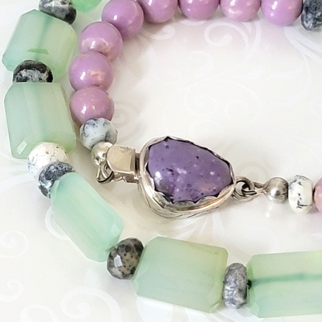 Close-up view of light green and purple stone beads and silver box clasp on a necklace.