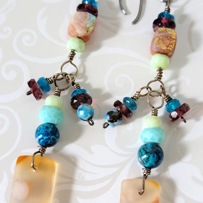 Close-up view of garnet, apatite, sunstone, and shattuckite beads on dangle earrings.