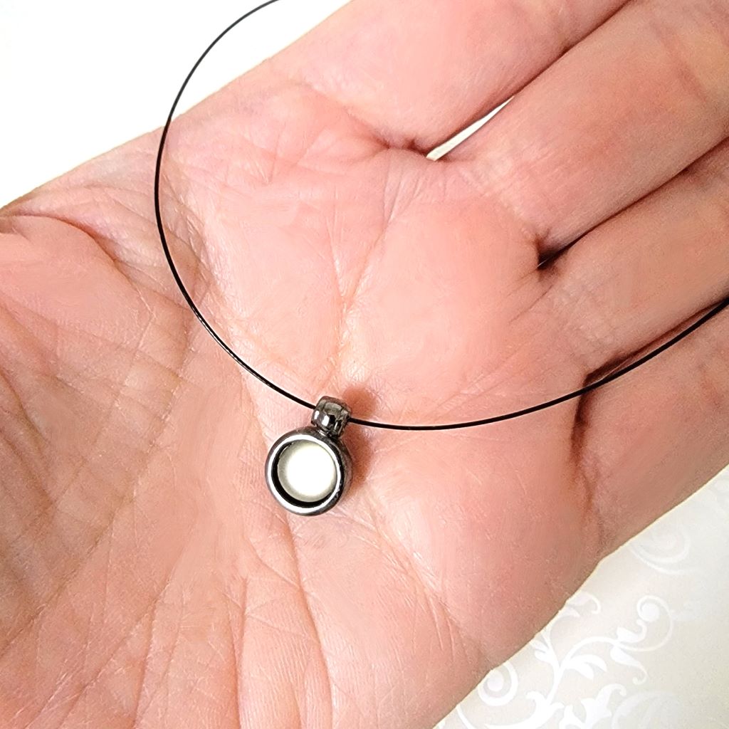 Closeup view of a skinny Express choker with a small glass pendant. Shown in hand, for size comparison.