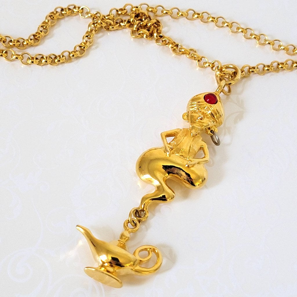 Closeup view of a gold tone Liz Claiborne genie pendant, with dangling bottle charm.
