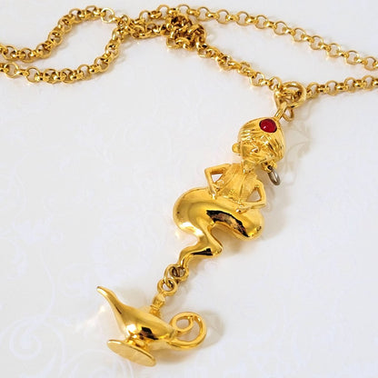 Closeup view of a gold tone Liz Claiborne genie pendant, with dangling bottle charm.