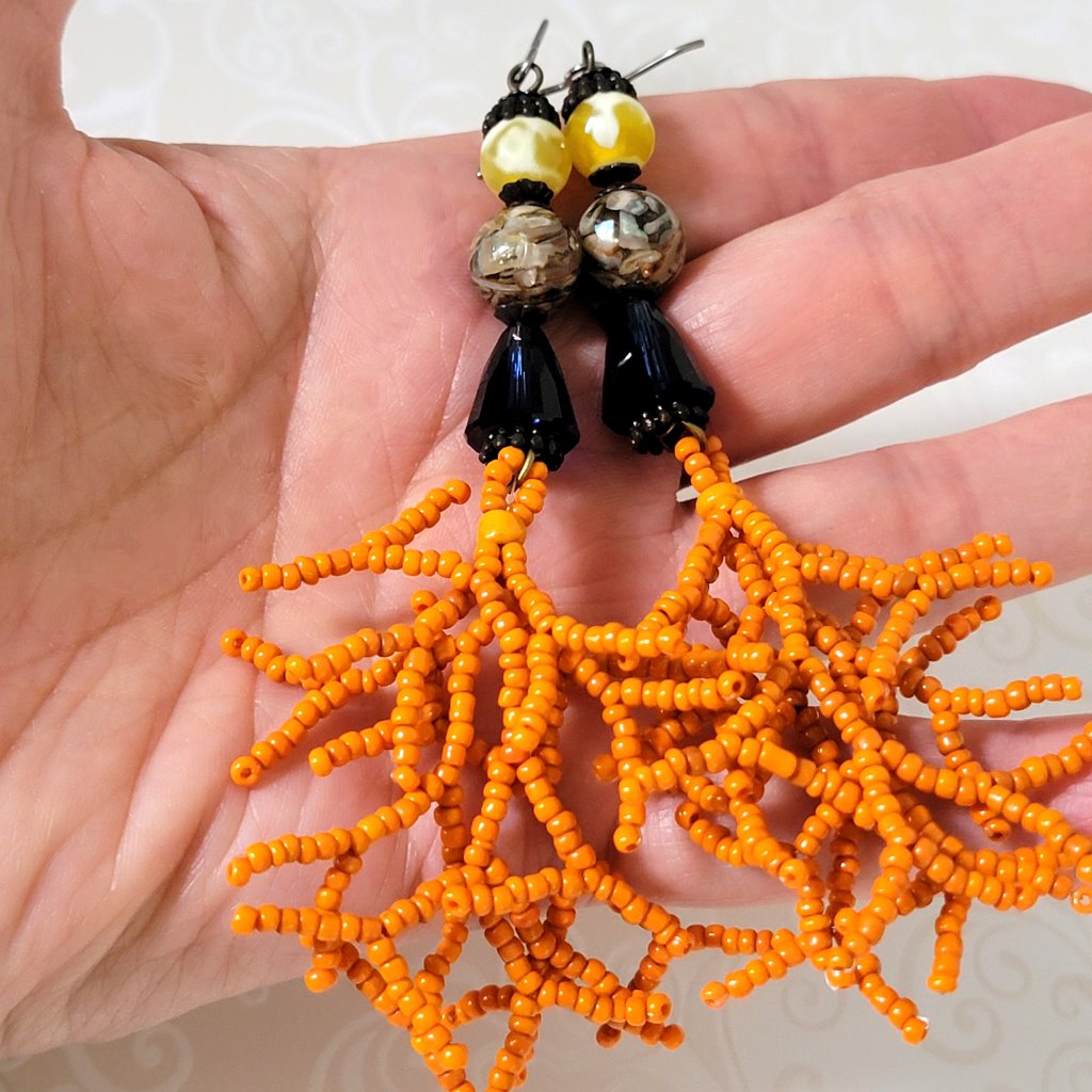 Long dangle earrings with yellow stones, blue crystals and orange seed bead branches. Shown in hand, for size comparison.