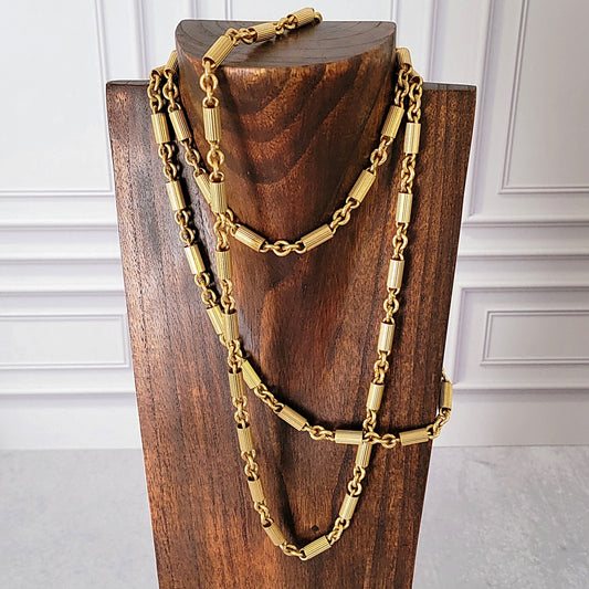 Long gold tone chain necklace on a wooden stand.
