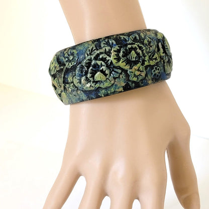 Goth style wide flower bracelet, in black molded resin, with green highlights. Shown on wrist.