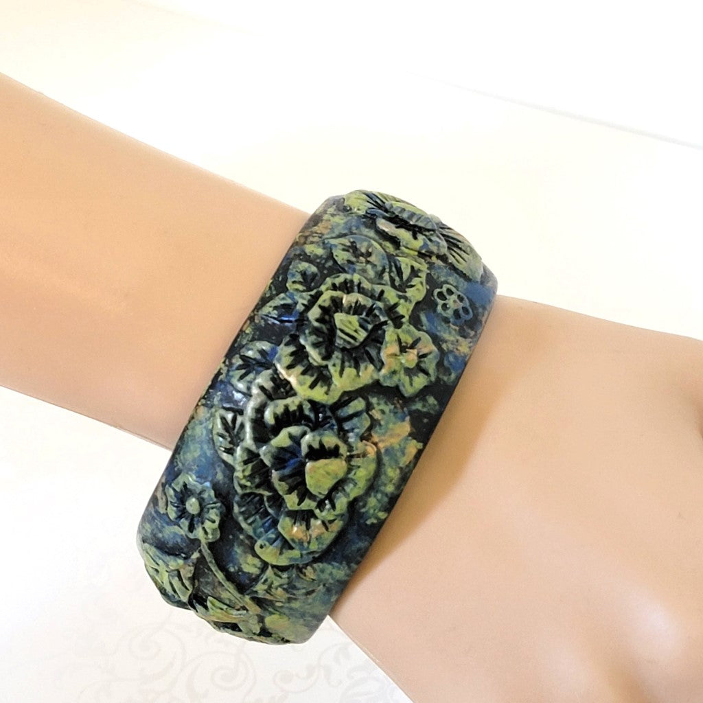 Boho style, big flower bracelet, in black molded resin, with green highlights. Shown on  a wrist.