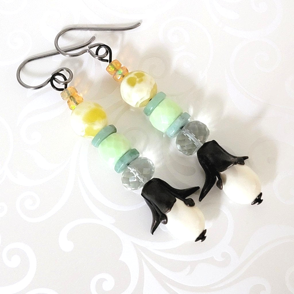 Long white floral drop earrings, with black petals, yellow and green gemstones, and tiny opals.