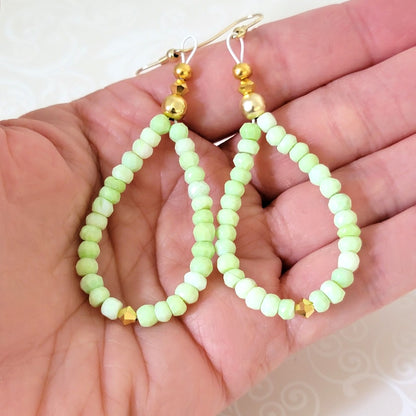 Handmade green opal beaded loop earrings, shown in hand, for size comparison.