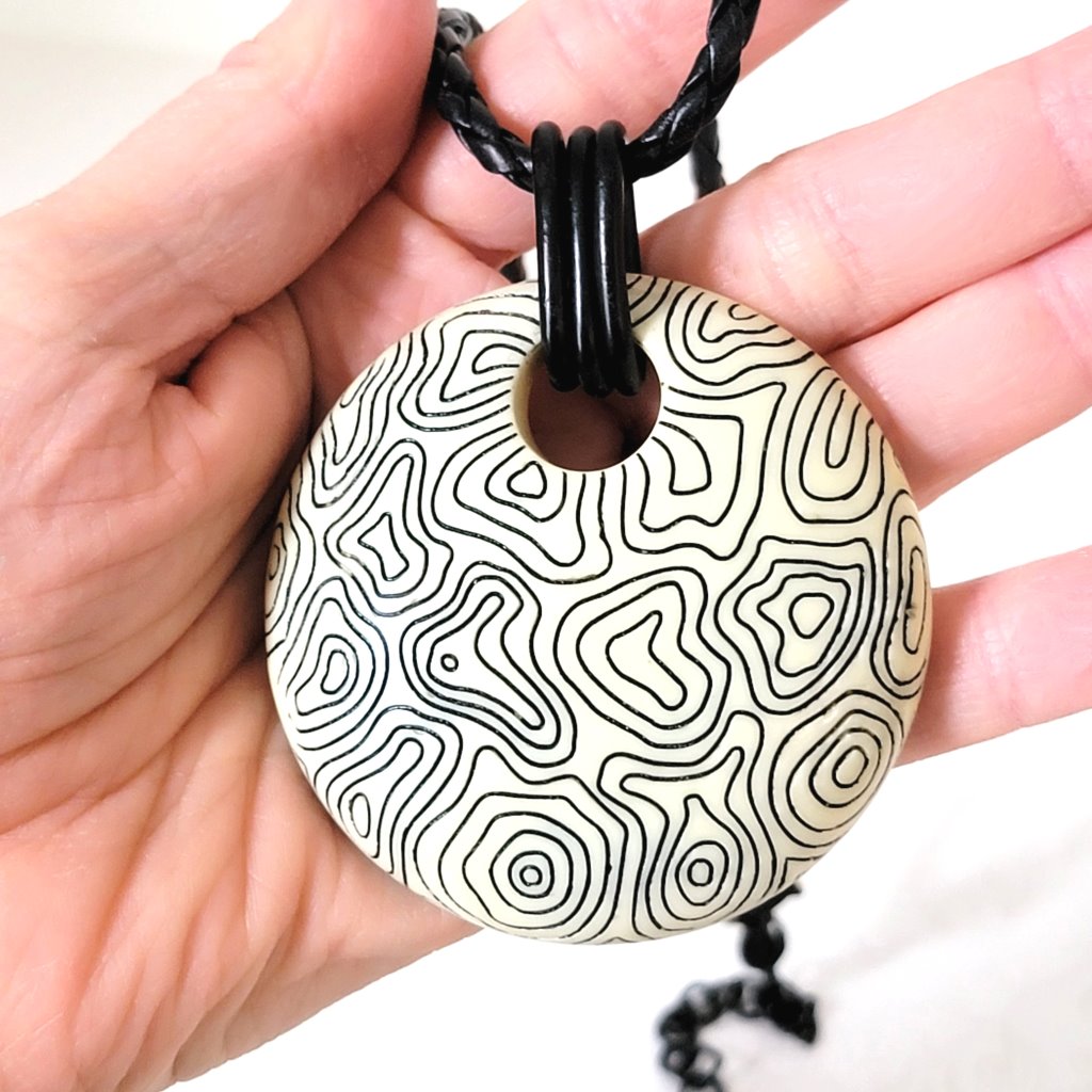 Large circle pendant, cream resin, with abstract black swirl line pattern, shown in hand, for size comparison.