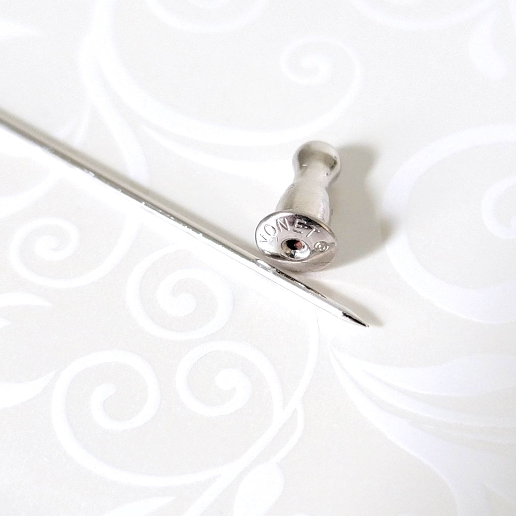 Pointed end of a Monet stick pin, with its clutch, showing signature mark.