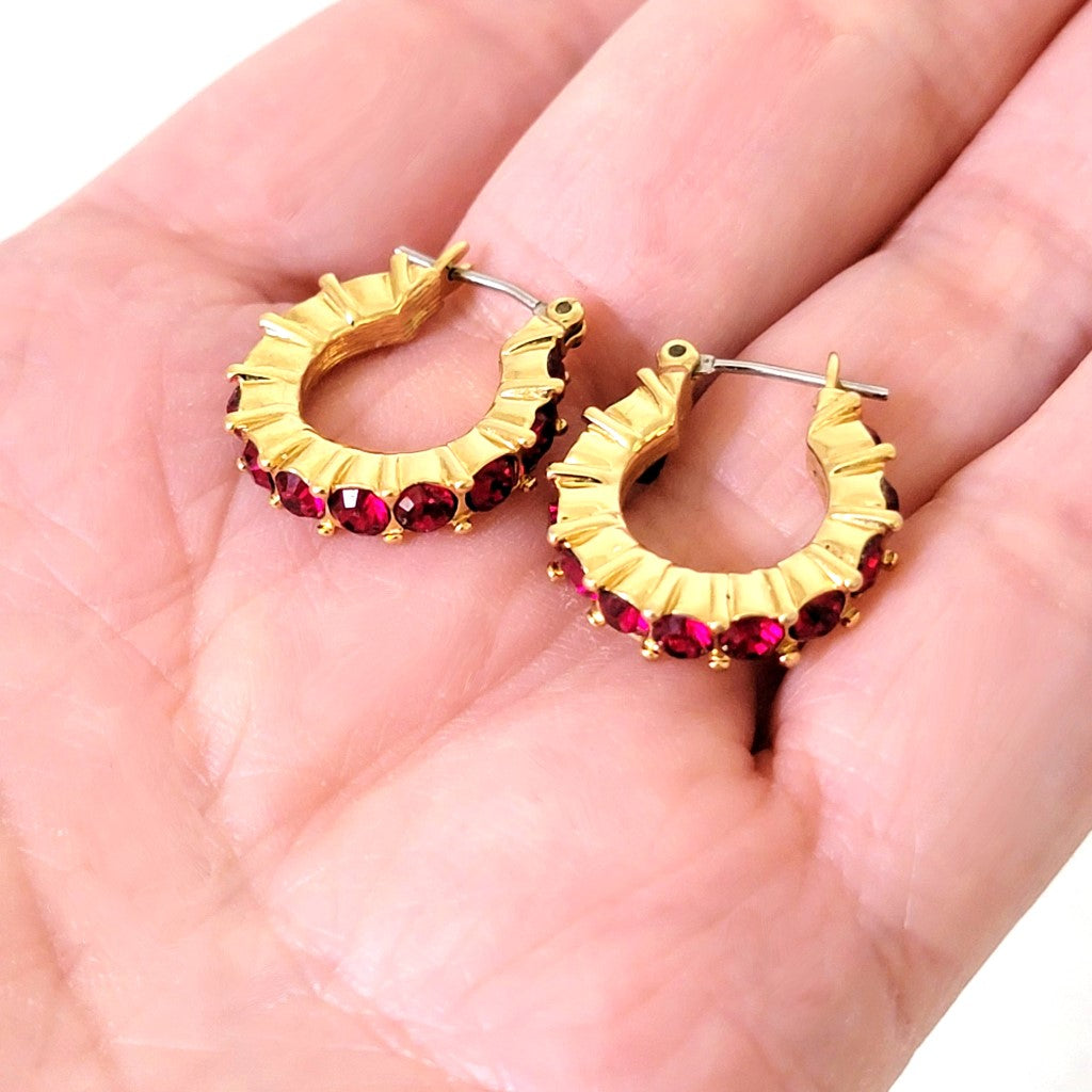 Napier gold tone and red rhinestone hoop earrings, shown in hand, for size comparison.