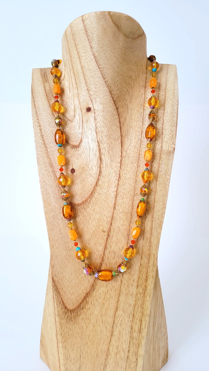 Orange long beaded necklace on display stand.
