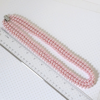 Vintage pink faux pearl necklace, next to a ruler.