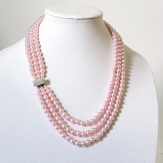 Pink three strand faux pearl necklace, with rhinestone clasp, on a display stand.