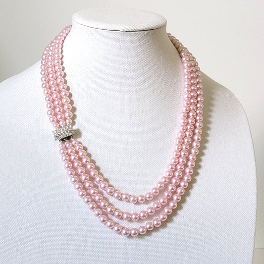 Pink three strand faux pearl necklace, with rhinestone clasp, on a display stand.