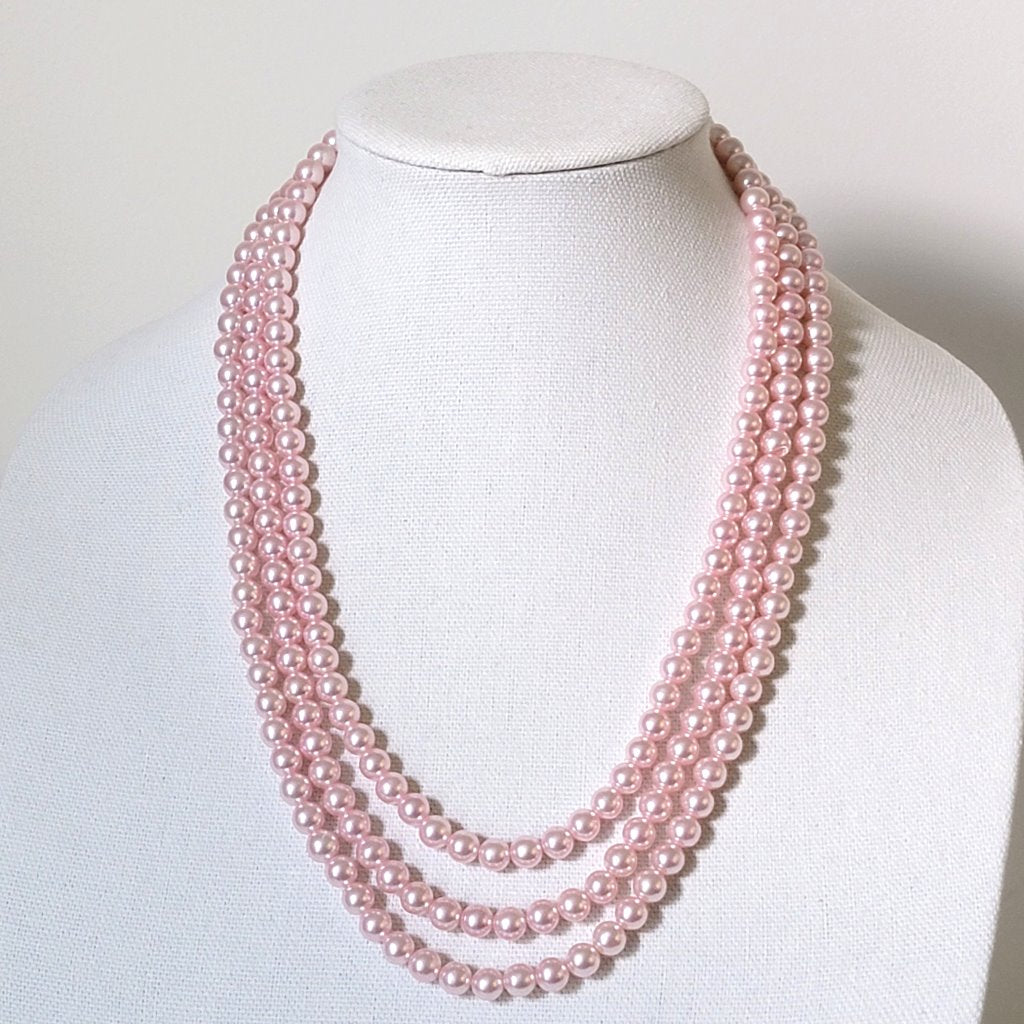 Pink vintage three strand faux pearl necklace on display.