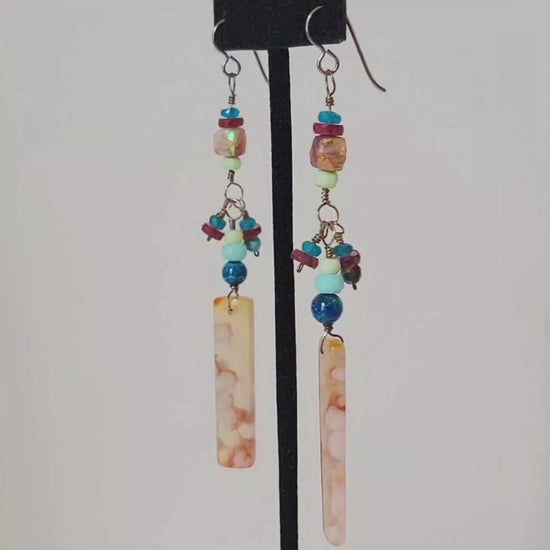 Video of a pair of very long gemstone dangle earrings, in shades of peach and blue.