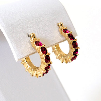 Napier red rhinestone, gold tone, small hinged hoop earrings, shown on a display stand.