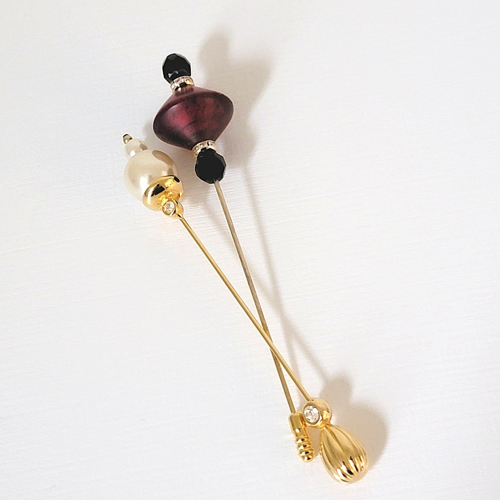 Two vintage stick pins. One faux pearls and the other black and red glass.