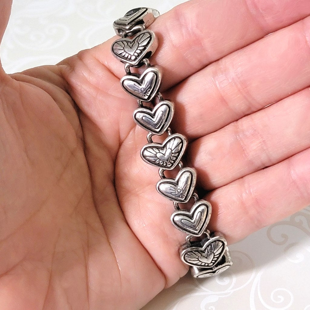 Close-up view of a Brighton hearts link bracelet, in silver tone, shown in hand, for size comparison.