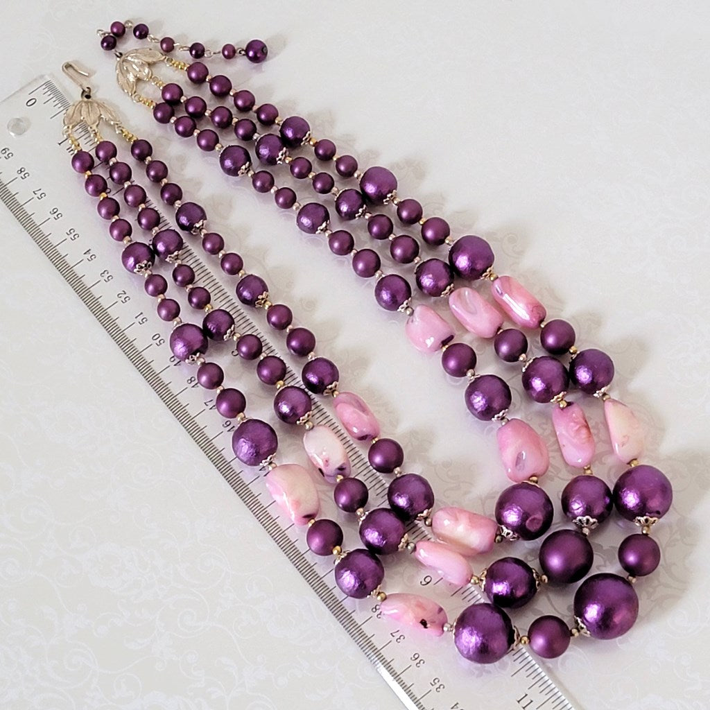 Three strand faux pearl necklace next to a ruler.