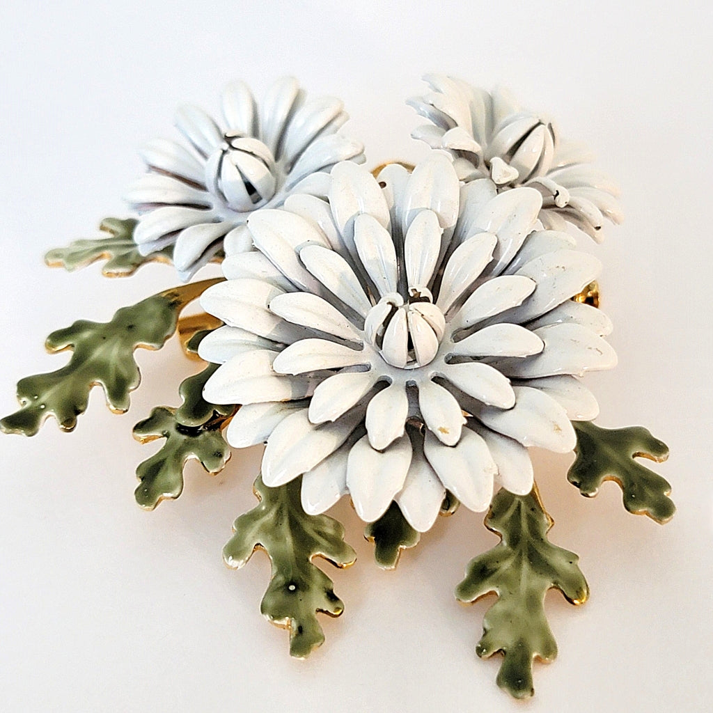 Vintage white enamel flower brooch with green leaves.