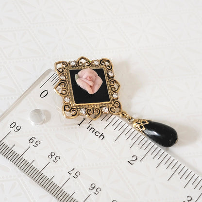 1928 black dangle and pink rose brooch, next to a ruler.